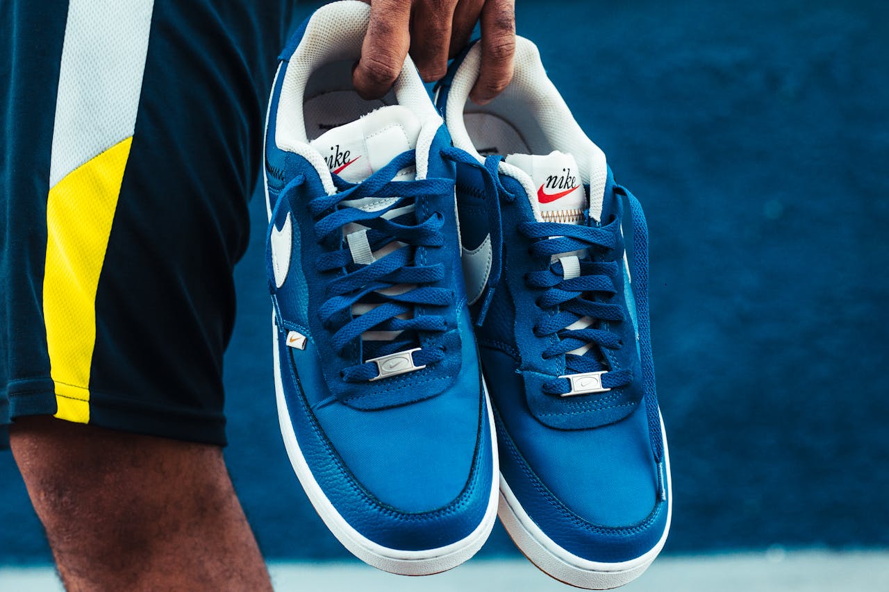 Detailed view of blue Nike sneakers being held outdoors, showcasing style and brand.