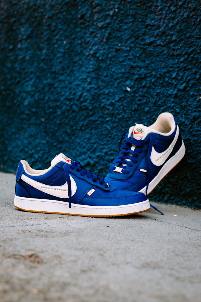 Stylish blue sneakers with white swoosh in focus against a blue textured wall.