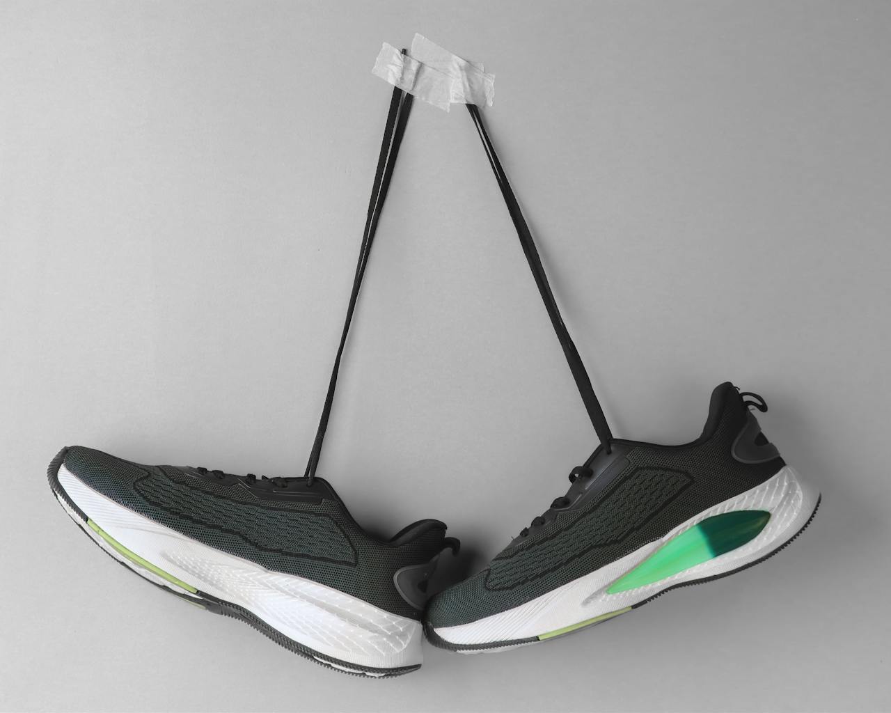 Stylish black and green running shoes creatively hung on a grey wall, showcasing modern design.